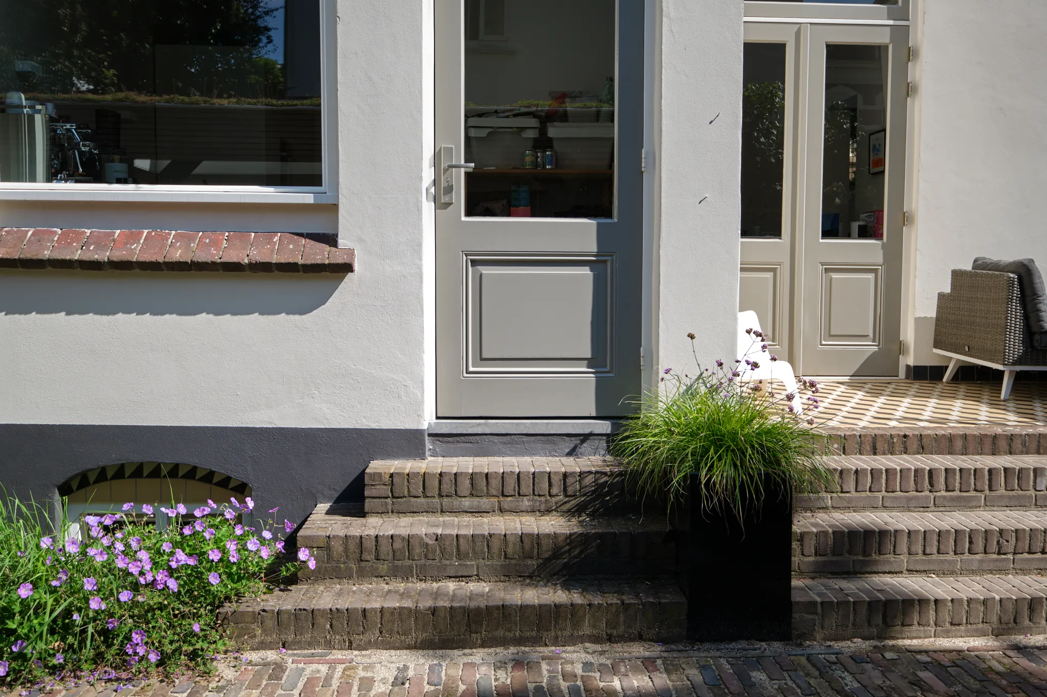 Voorkant met bakstenen trappen, paarse bloemen en moderne glazen deuren