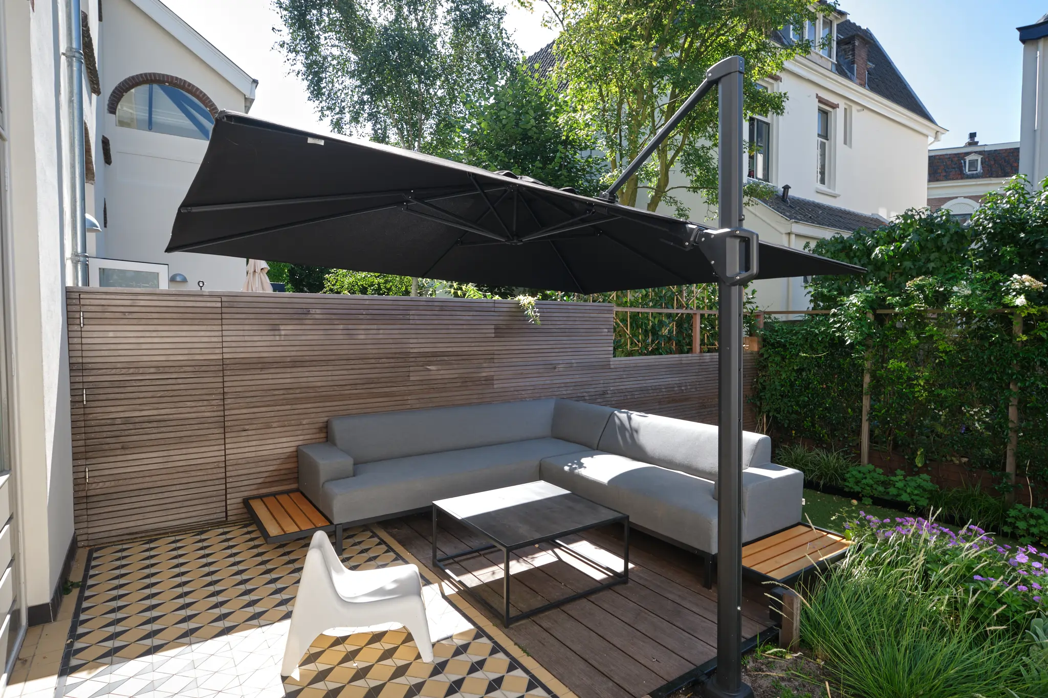 Moderne lounge hoek met grijze zitbank, glazen tafel en grote parasol