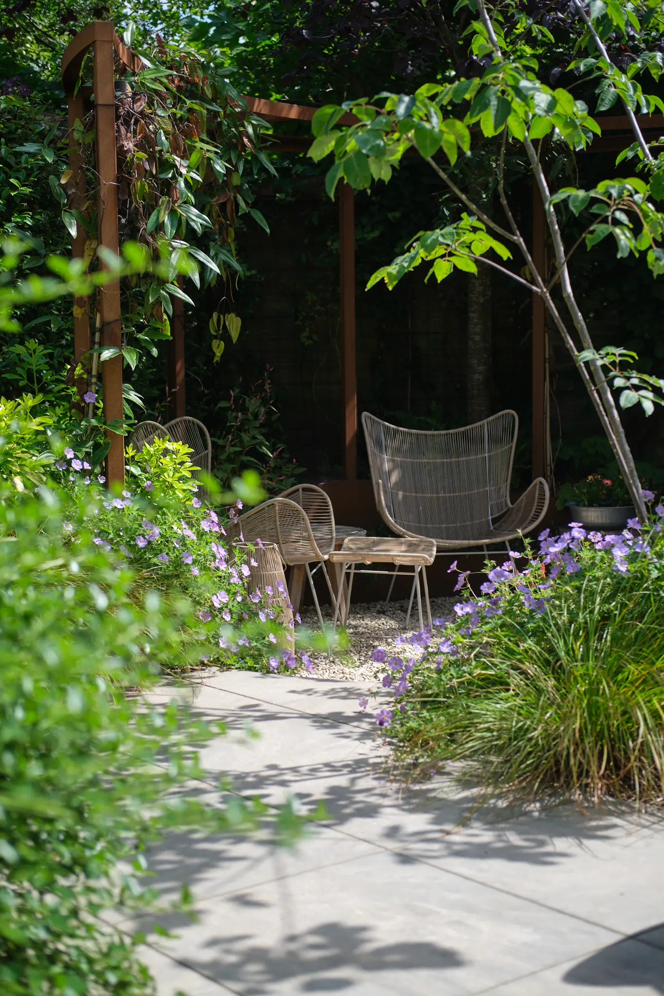 Intieme zithoek onder houten pergola met paarse bloeiende planten