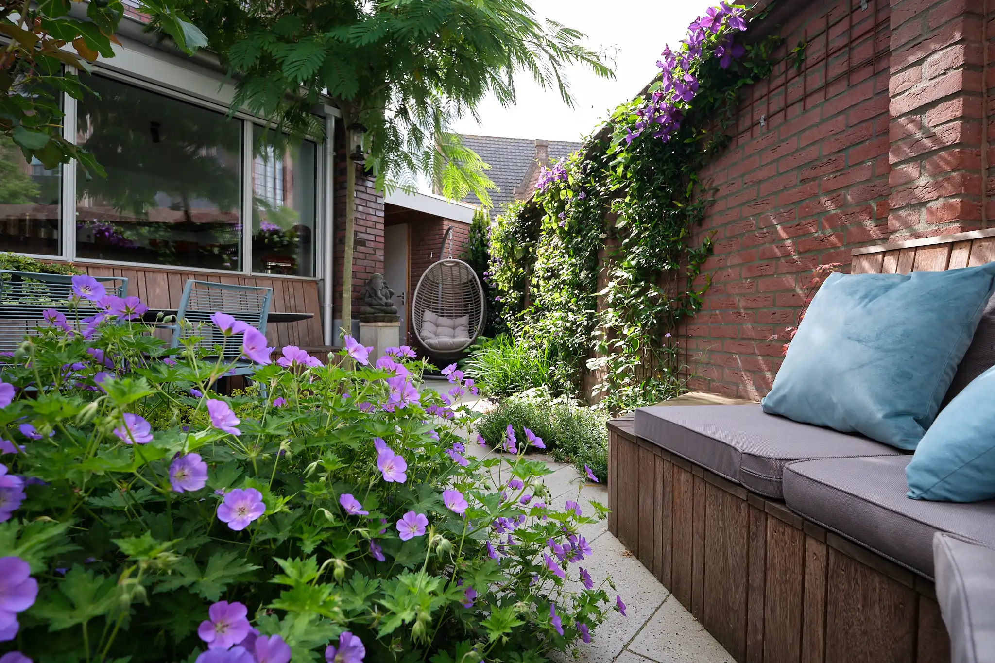 Compleet overzicht van de intieme tuinhoek met paarse bloemen en zithoeken