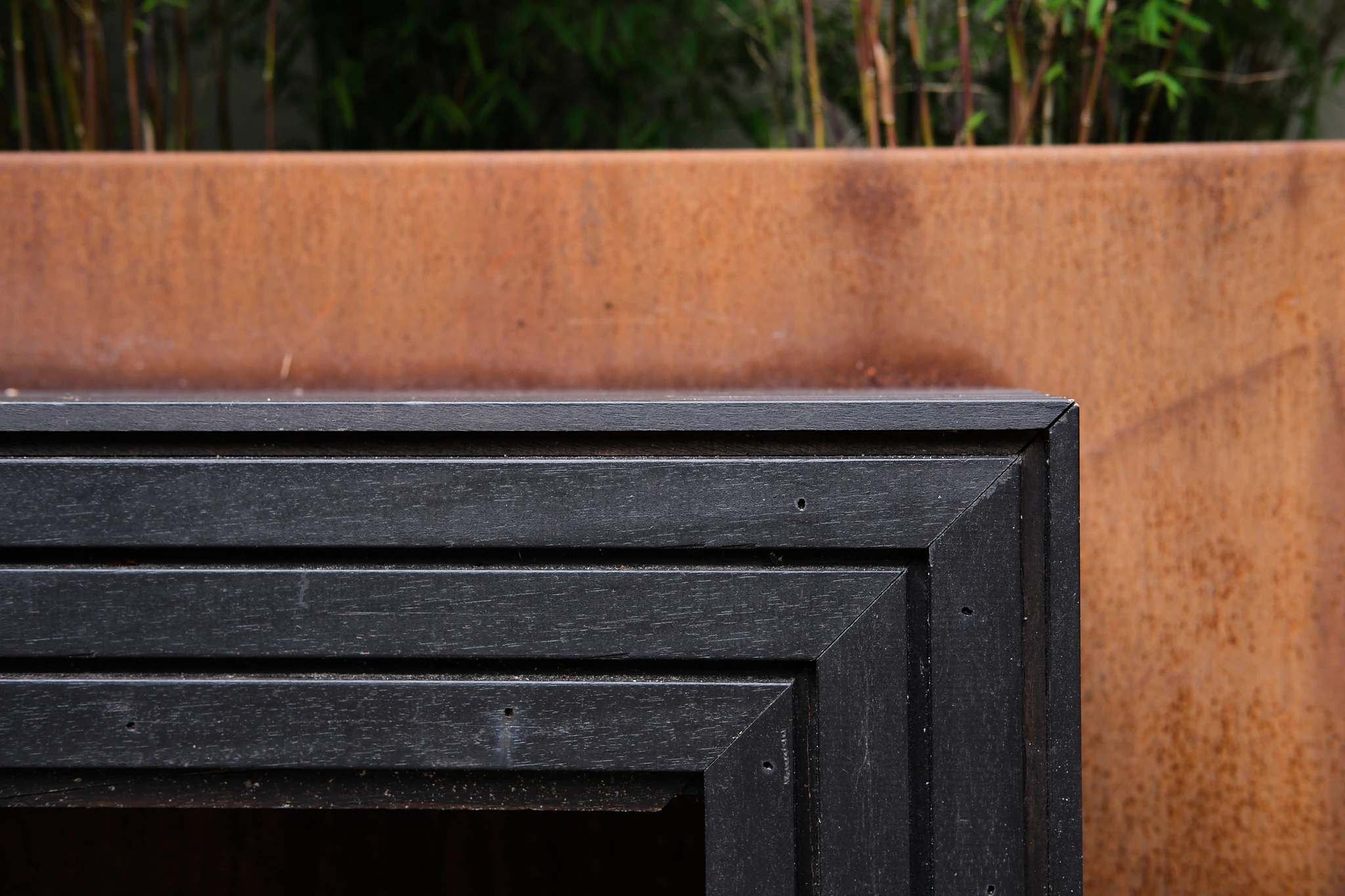 Detail van zwarte houten latwerk met corten staal rand