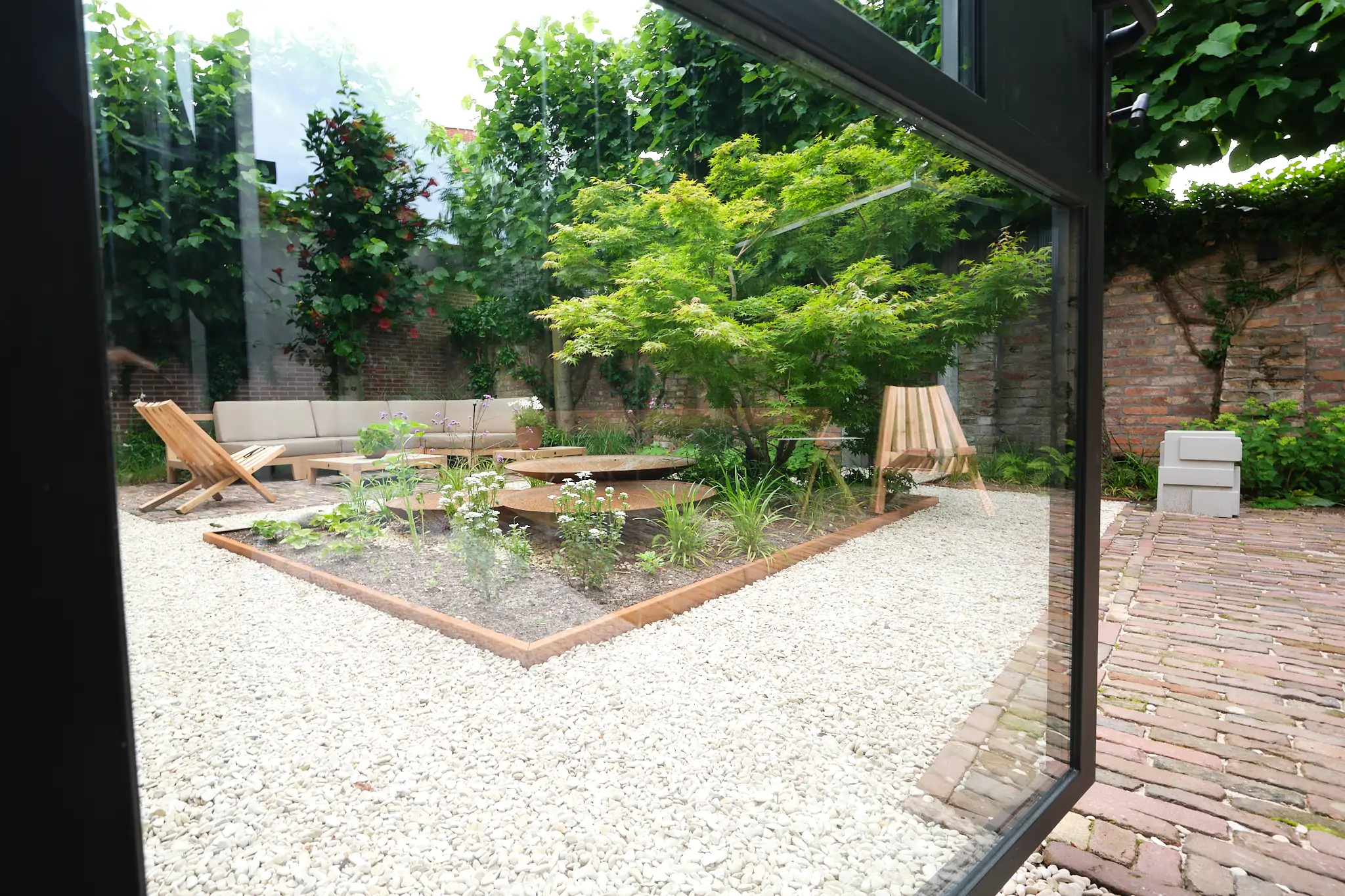 Uitzicht vanuit binnen naar minimalistische tuin met geometrische plantenbakken